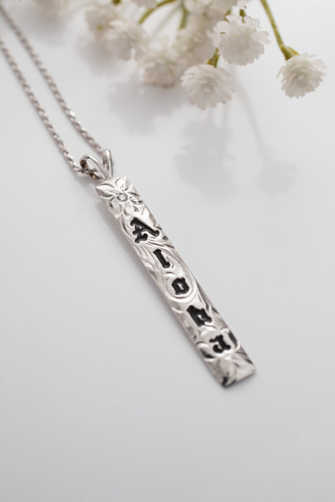 White gold vertical Hawaiian pendant with "Aloha" in black enamel lettering.